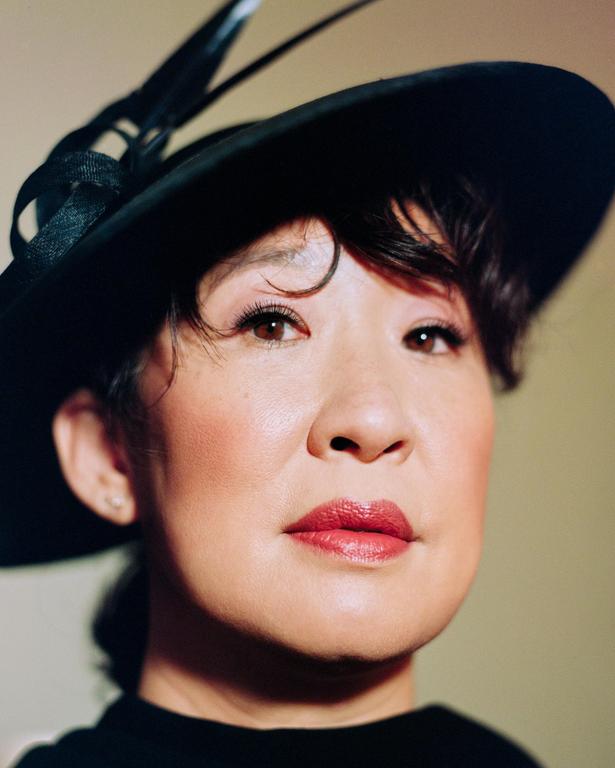 A woman wearing a black hat with feathers looks directly at the viewer.