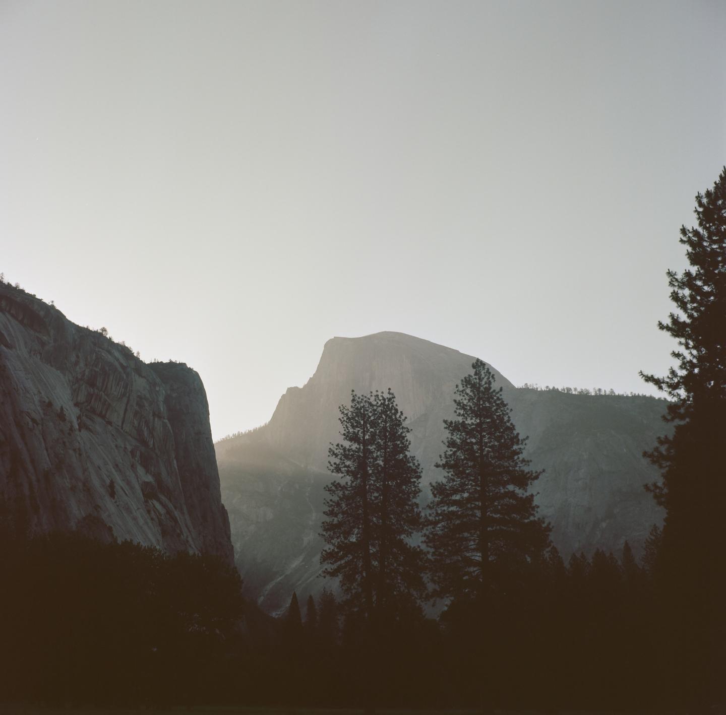 Sunlight illuminates a mountain peak behind silhouetted trees and a valley.