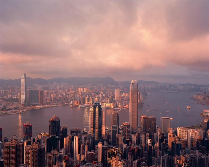 An aerial view of a city with many skyscrapers and a body of water with boats, under a cloudy sky.