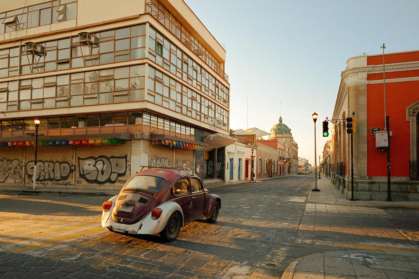 A two-tone car is parked on a cobblestone street in a city with colorful buildings and a clear sky.