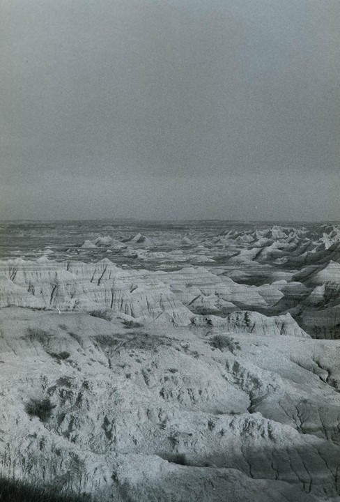 A vast landscape of eroded hills and valleys stretches under a cloudy sky.