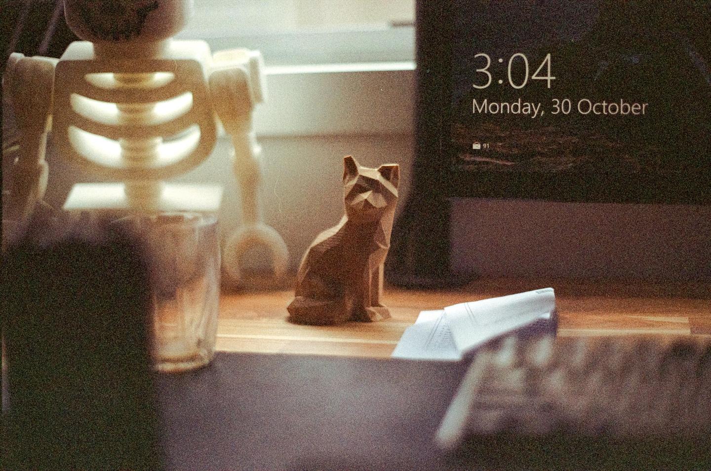 A wooden cat figurine sits on a desk next to a computer screen displaying the time and date.