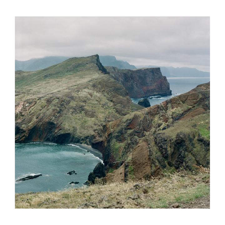 A dramatic landscape shows a rugged coastline with steep cliffs meeting the ocean under a cloudy sky.