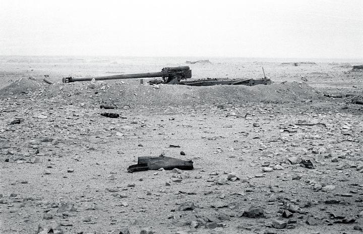 A destroyed Iraqi artillery battery is visible on a rocky, barren landscape under a bright sky.