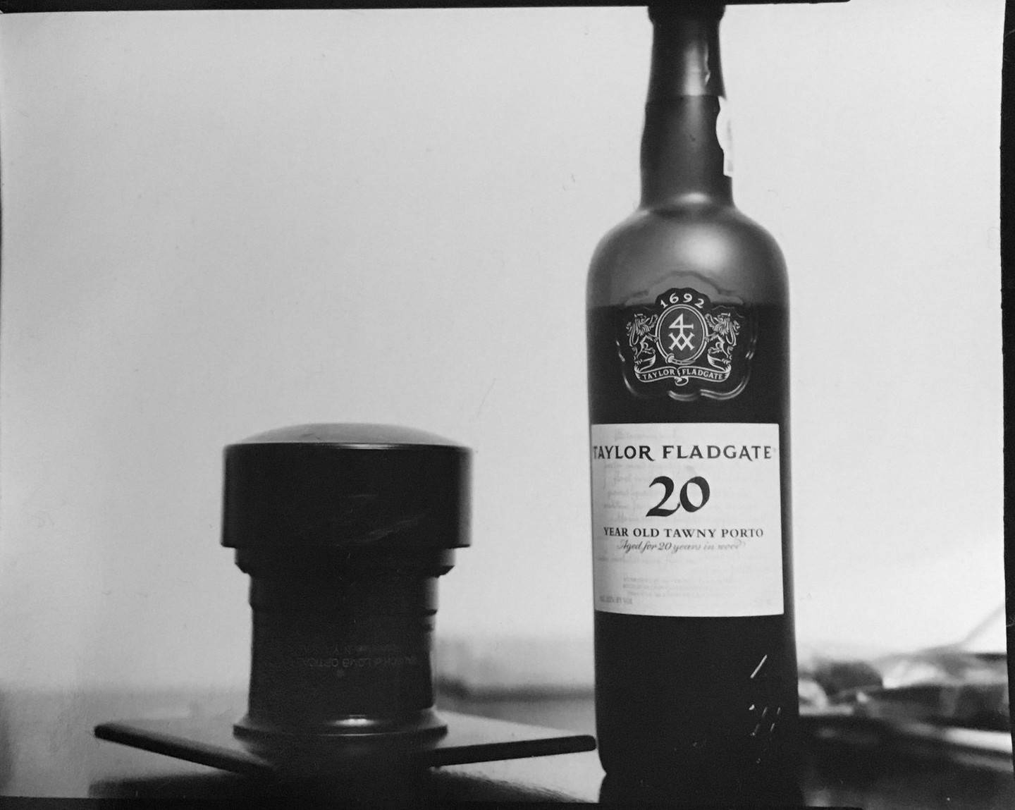A bottle of Taylor Fladgate 20 Year Old Tawny Porto stands next to a dark, cylindrical object.