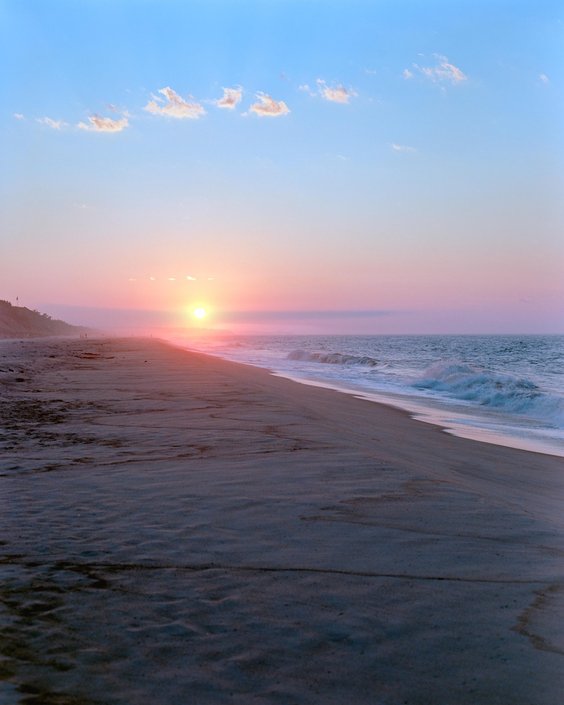 The sun rises over a beach with waves crashing on the shore.