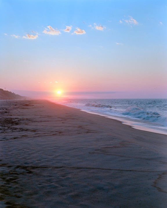 The sun rises over a beach with waves crashing on the shore.