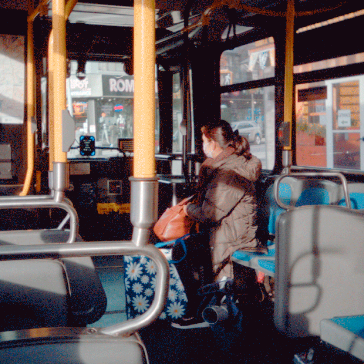 A woman wearing a face mask sits on a bus next to a window.
