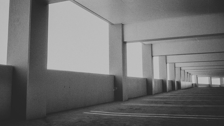 A long, empty parking garage hallway is illuminated by bright windows on the right.