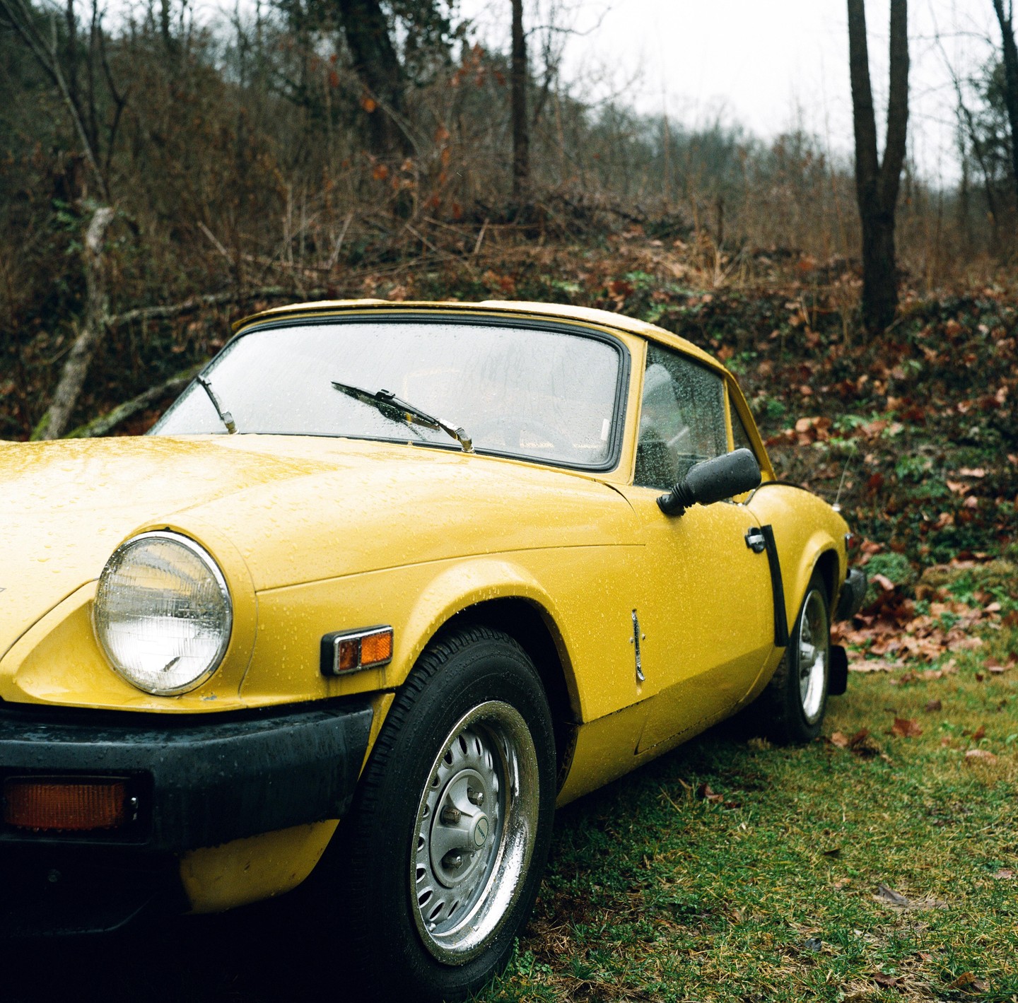 A yellow car is parked on a grassy area next to a forest.