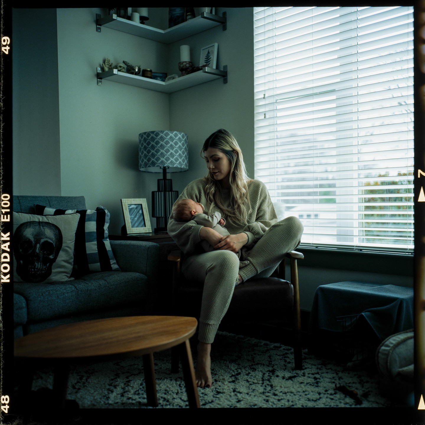 A woman sits in a chair holding a newborn baby in a living room.
