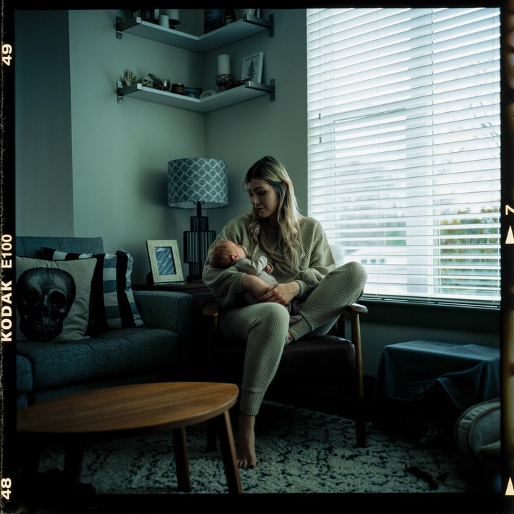 A woman sits in a chair holding a newborn baby in a living room.