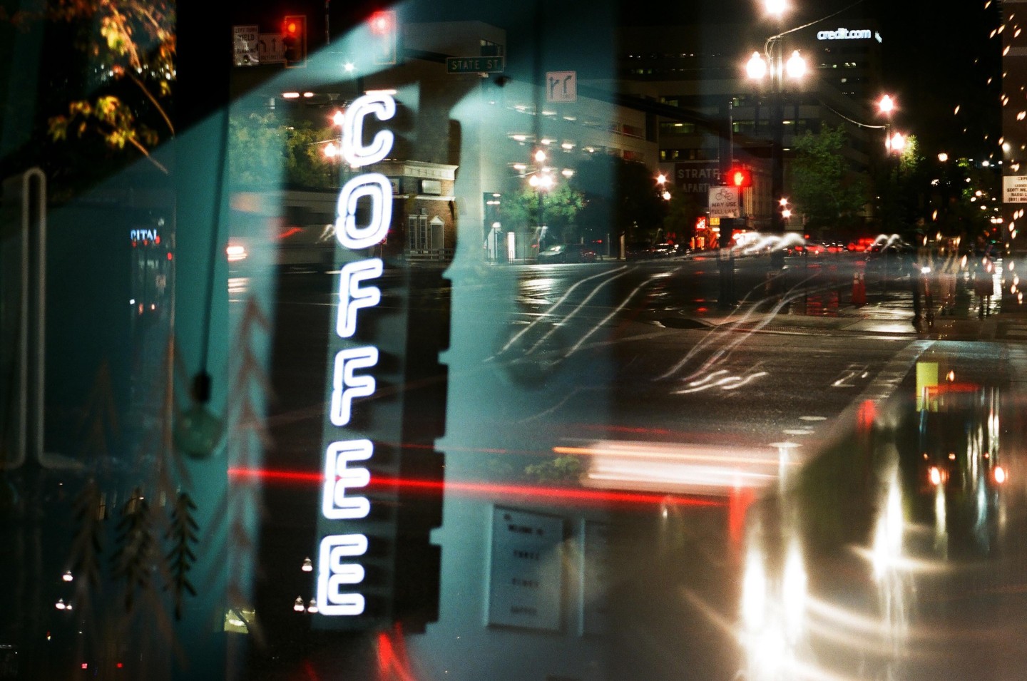 A neon "COFFEE" sign is reflected in a window overlooking a city street at night.