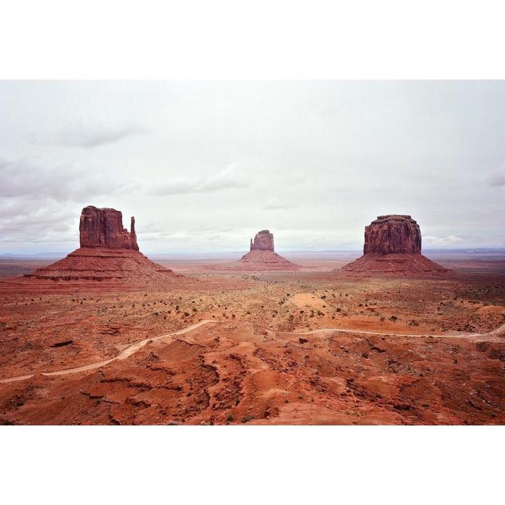 Three large rock formations stand in a vast desert landscape under a cloudy sky.