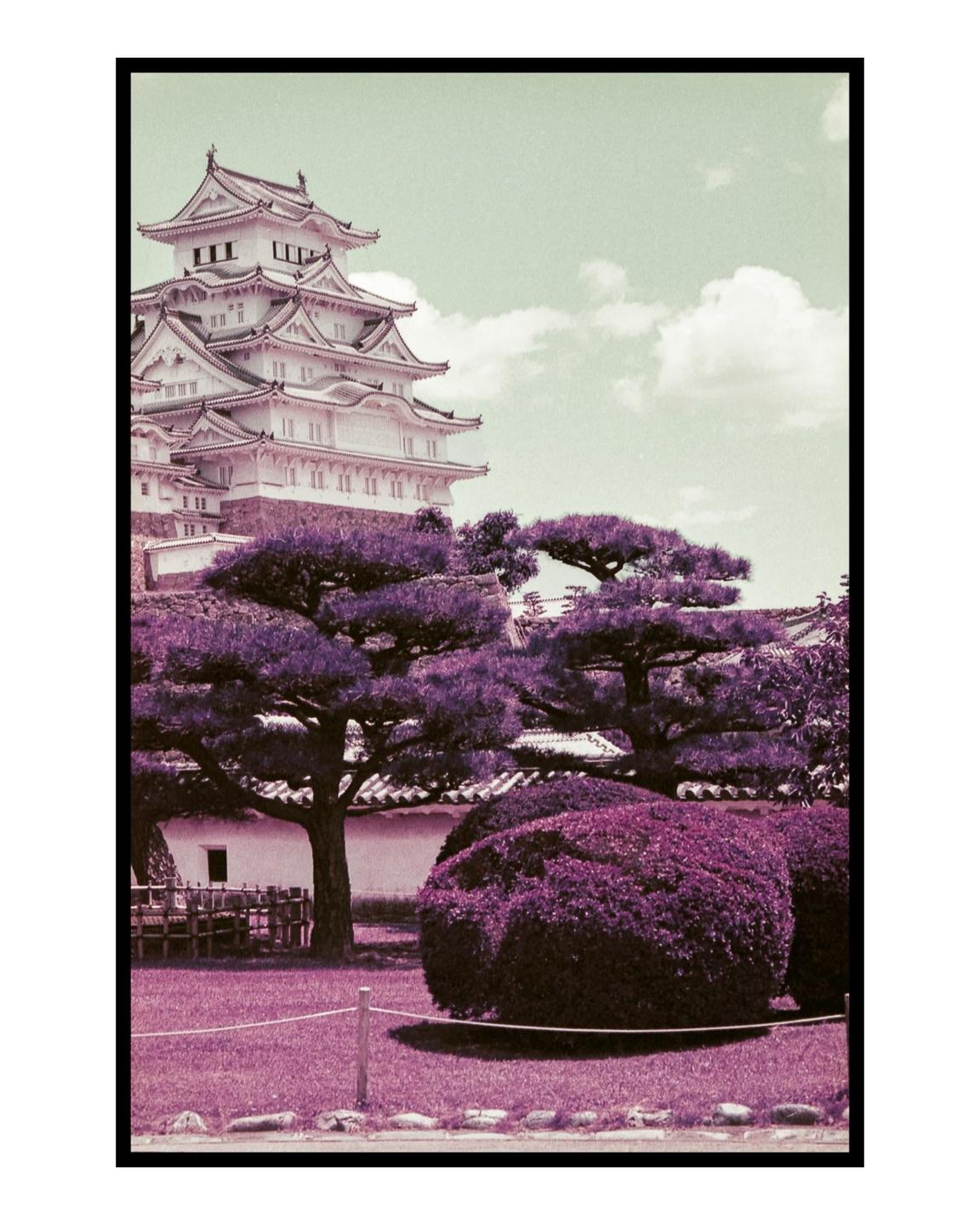 A large white multi-story castle with traditional Japanese architecture stands behind purple trees and bushes under a light green sky.