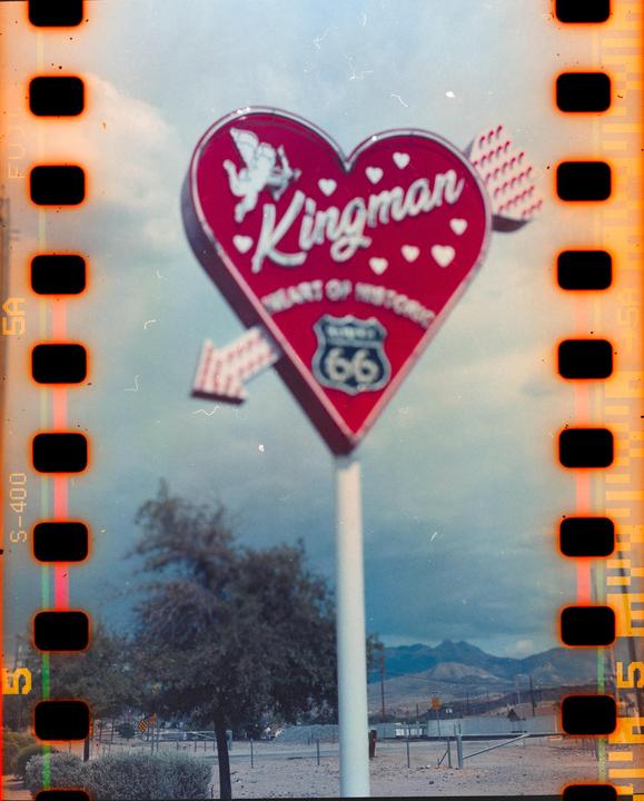 A heart-shaped sign for Kingman, "Heart of Historic Route 66," stands against a cloudy sky with mountains in the distance.