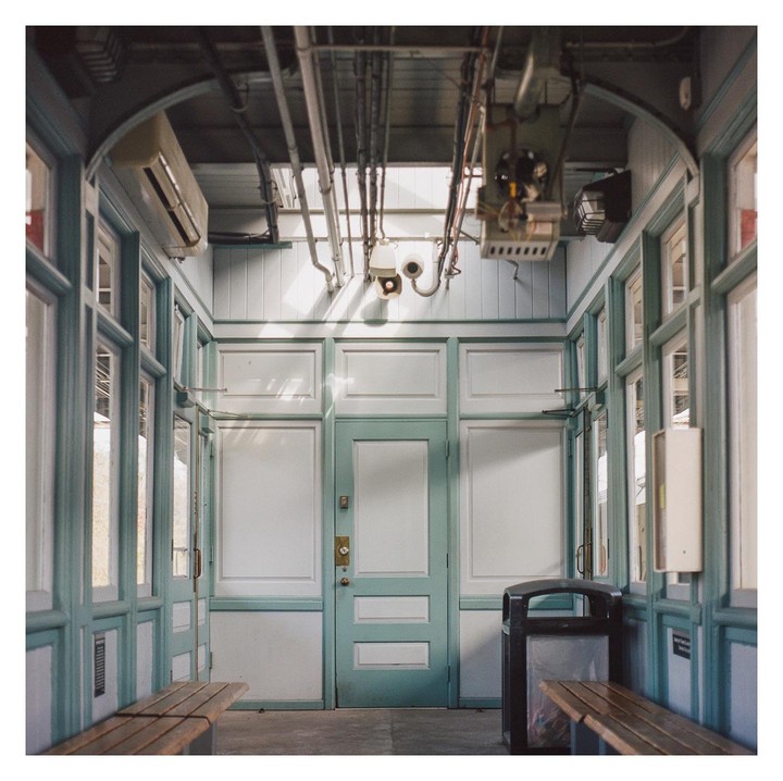 A waiting room with light blue trim and white panels features two wooden benches, a trash can, and exposed pipes on the ceiling.