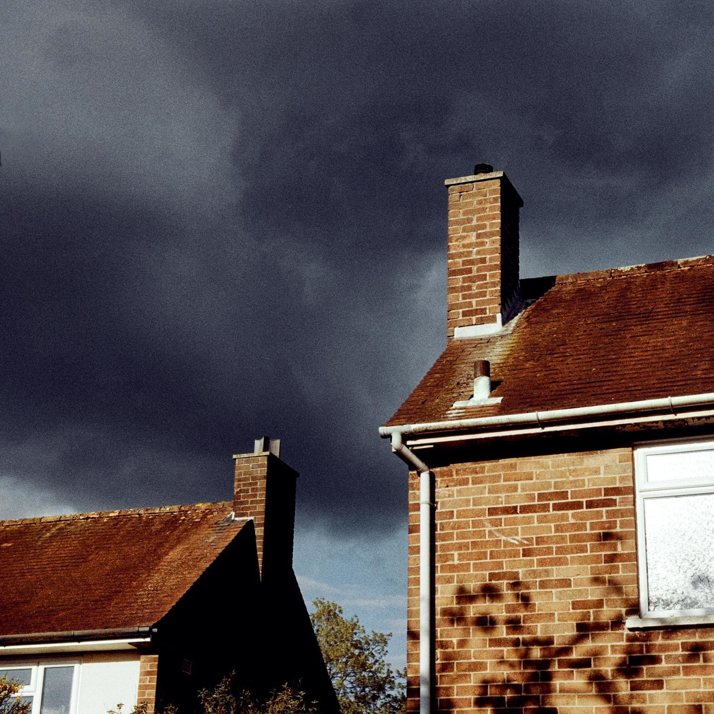 Two brick houses with red tile roofs are visible against a dark, cloudy sky.