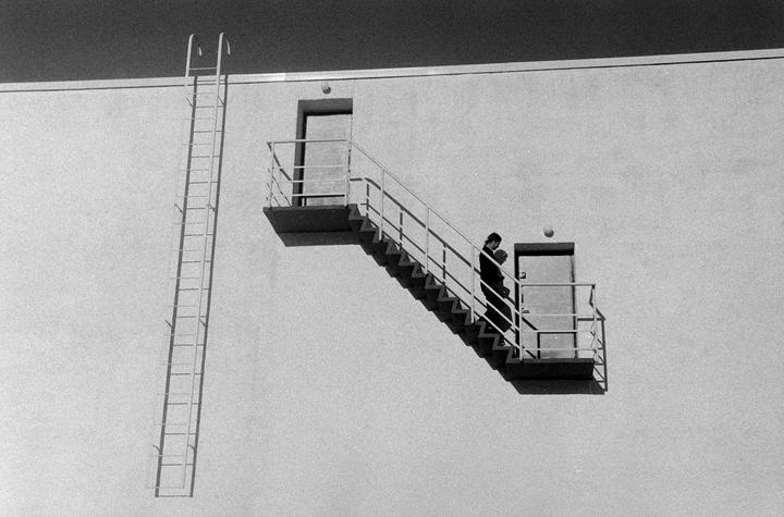 A woman descends an outdoor staircase on the side of a building, next to a tall ladder.