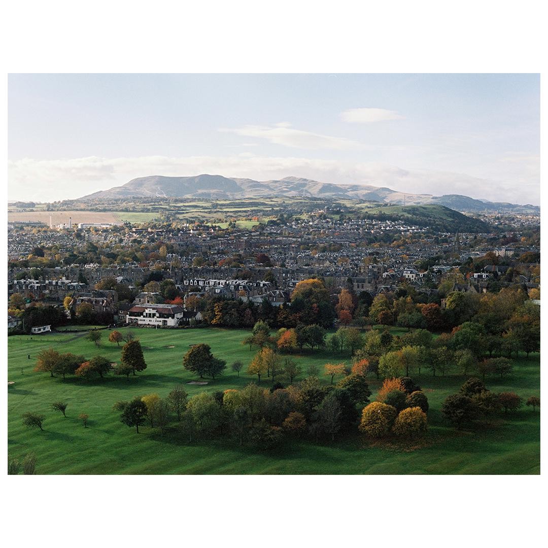 A golf course and a town are visible in the foreground, with mountains in the background.