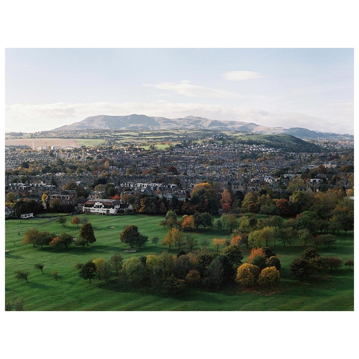 A golf course and a town are visible in the foreground, with mountains in the background.