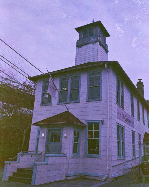 A white building with a tower and blue trim stands next to a bridge.