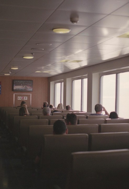 People sit in rows of seats inside a ferry looking out of the windows.