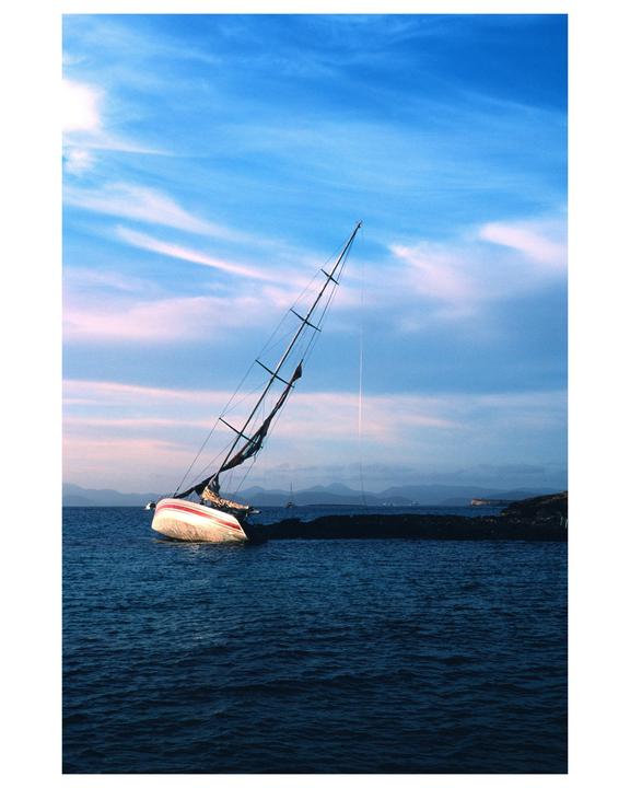 A sailboat is stranded on a rocky shore under a blue sky with wispy clouds.