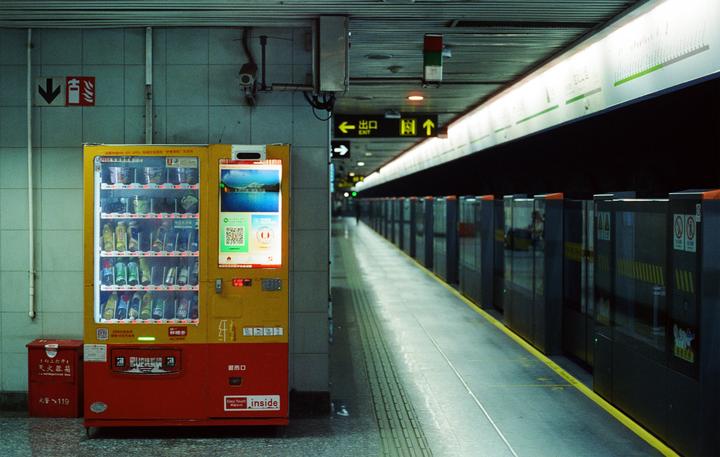 A brightly lit vending machine stands on a subway platform next to a long row of platform screen doors.