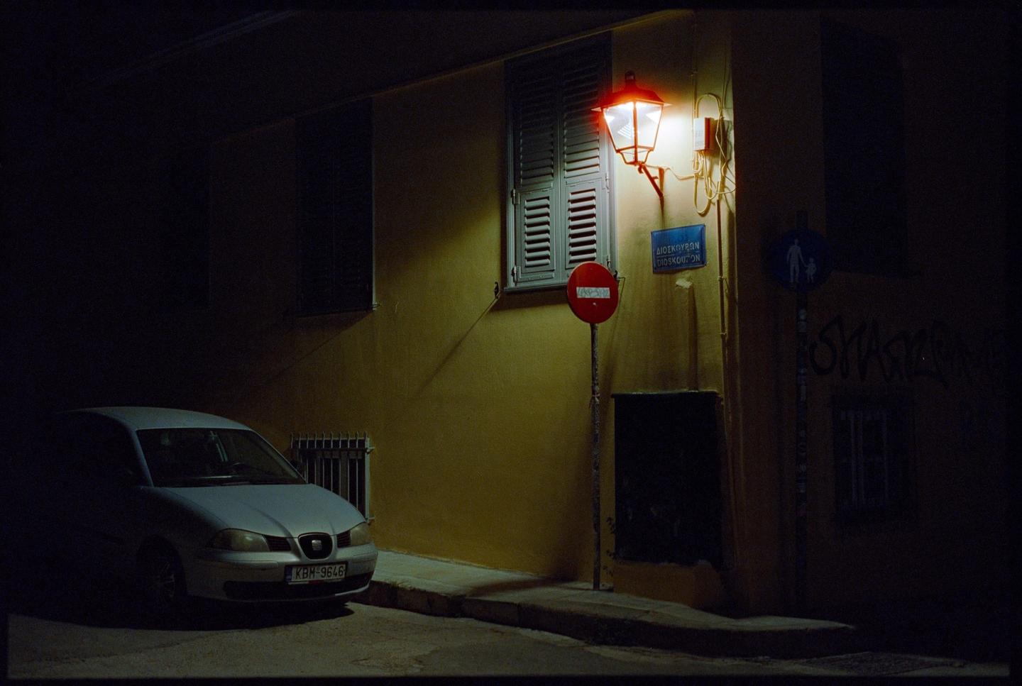A white car is parked on a dark street next to a building with a red lantern and a stop sign.