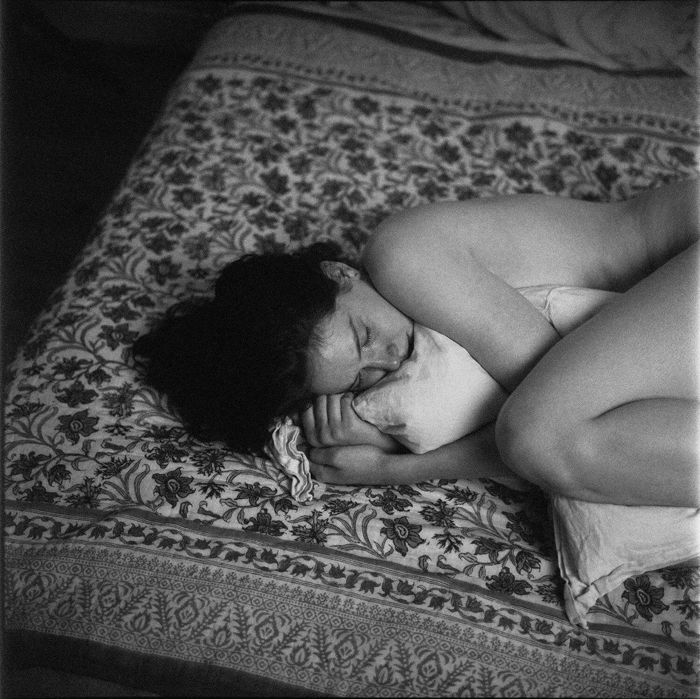 A woman sleeps curled up on a patterned bedspread.