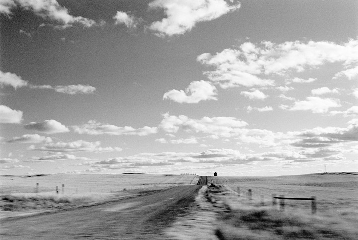 A long, straight road leads toward a distant building under a sky filled with clouds.