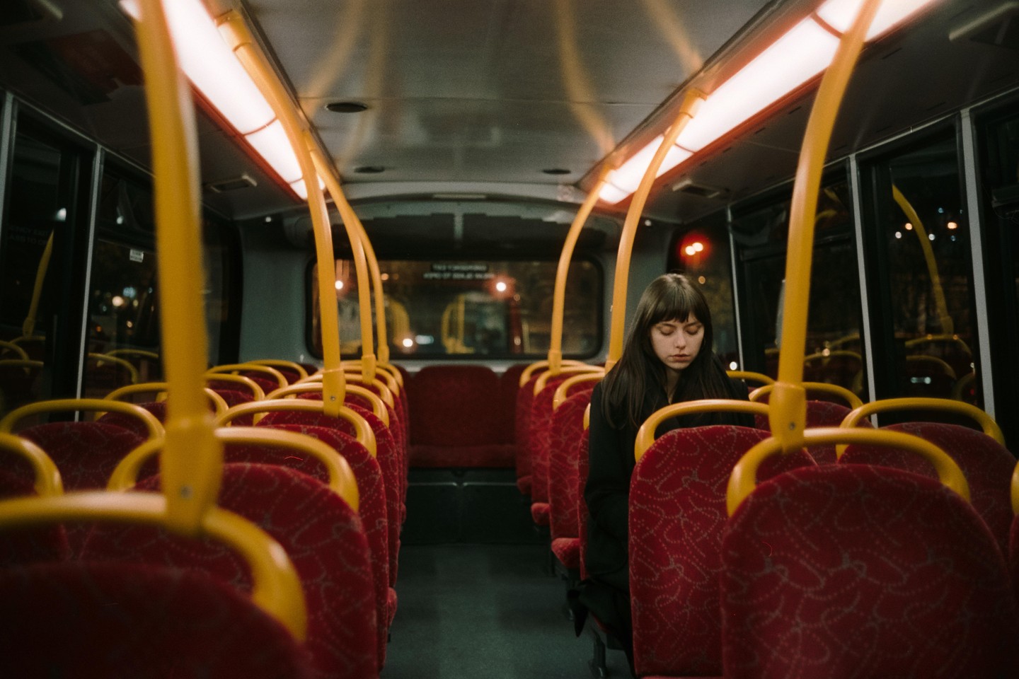 A woman with her eyes closed sits alone on a bus at night.