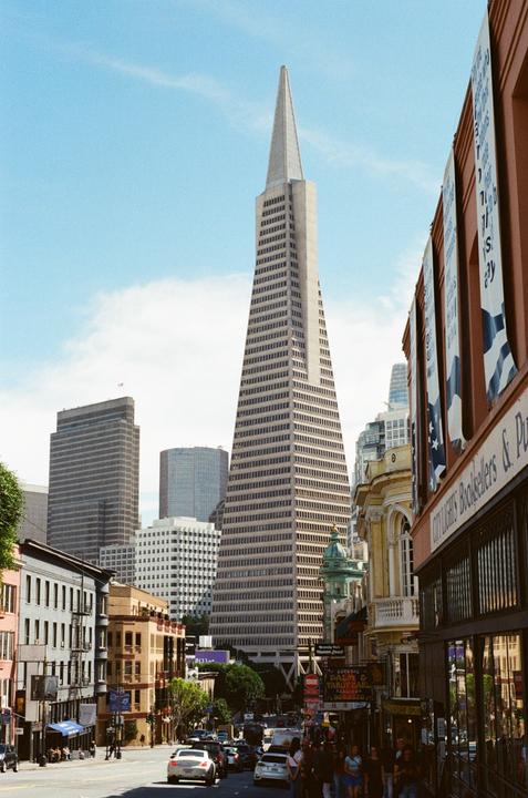 A tall, triangular skyscraper dominates the skyline above a busy city street with people and cars.