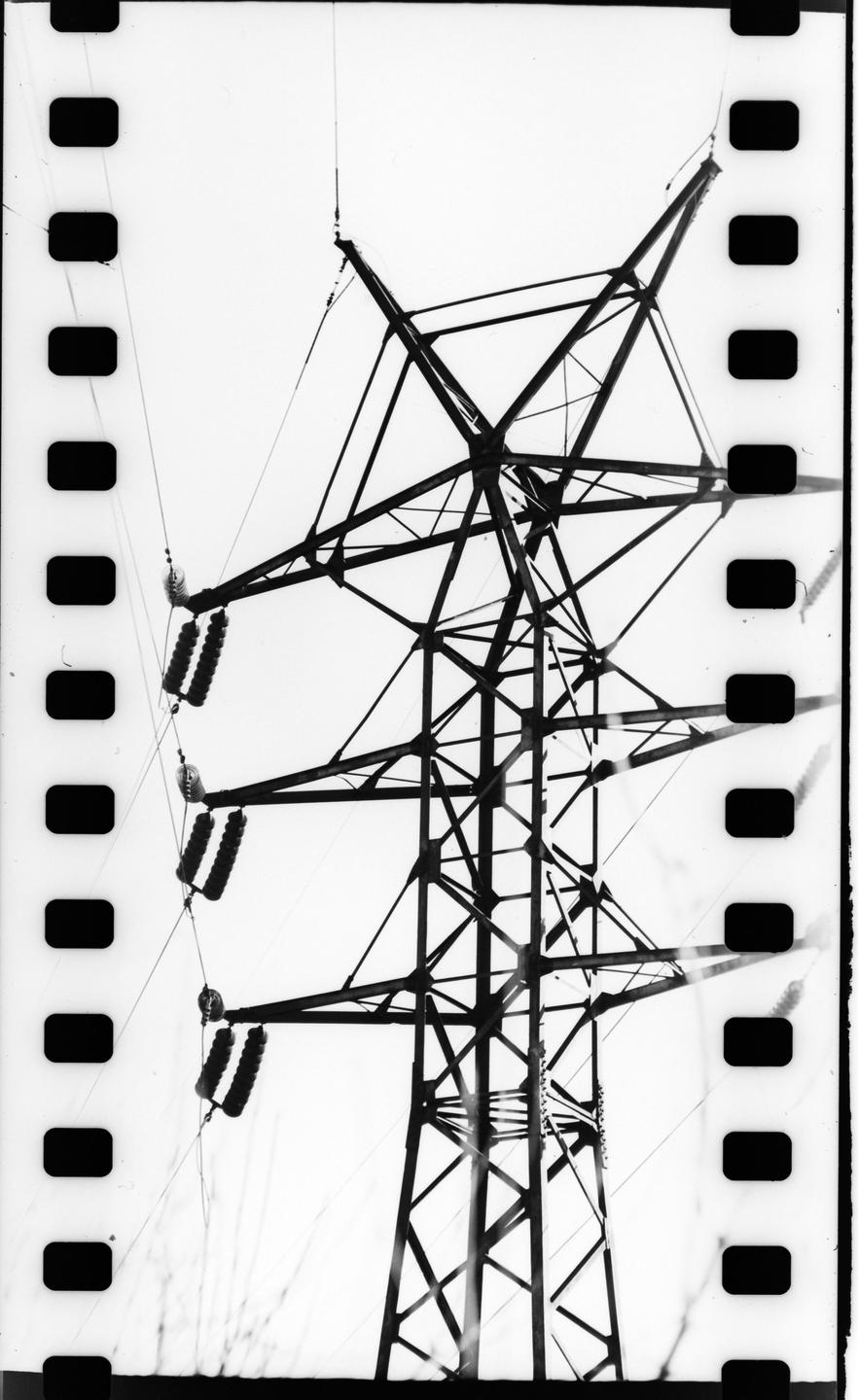 A black and white image shows a power line tower against a bright sky, with film sprockets visible on both sides.
