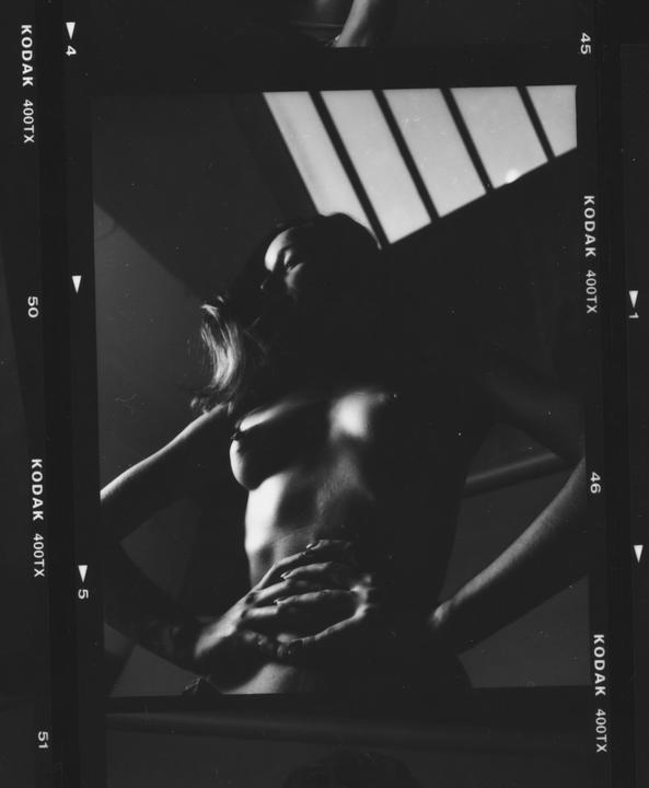 A woman stands with her hands on her hips, partially obscured by shadow, with light stripes on the wall behind her.