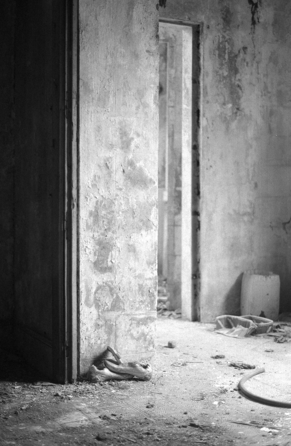 A long corridor with multiple doorways is visible through an open doorway in a derelict building.
