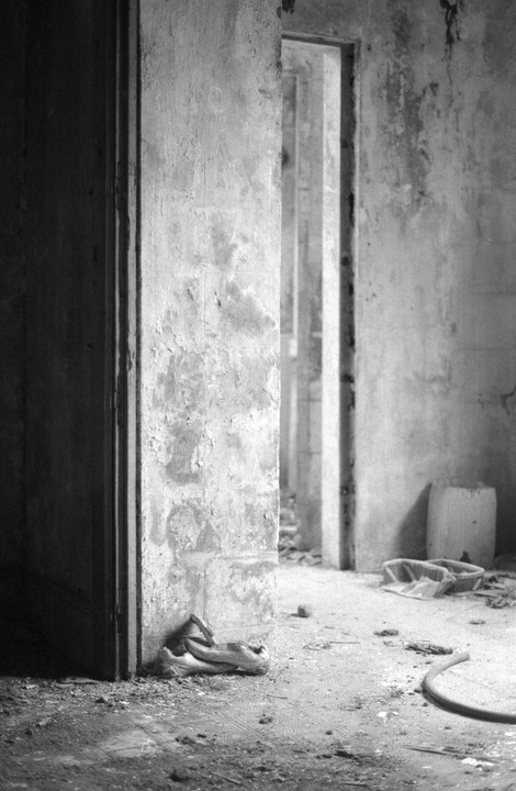 A long corridor with multiple doorways is visible through an open doorway in a derelict building.