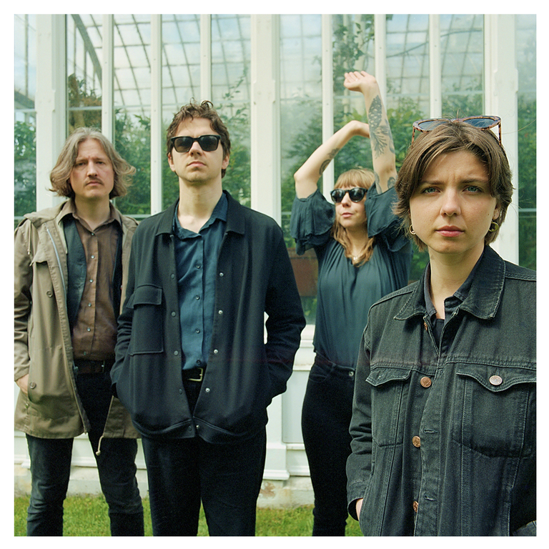 Four people stand in front of a greenhouse, two men and two women.