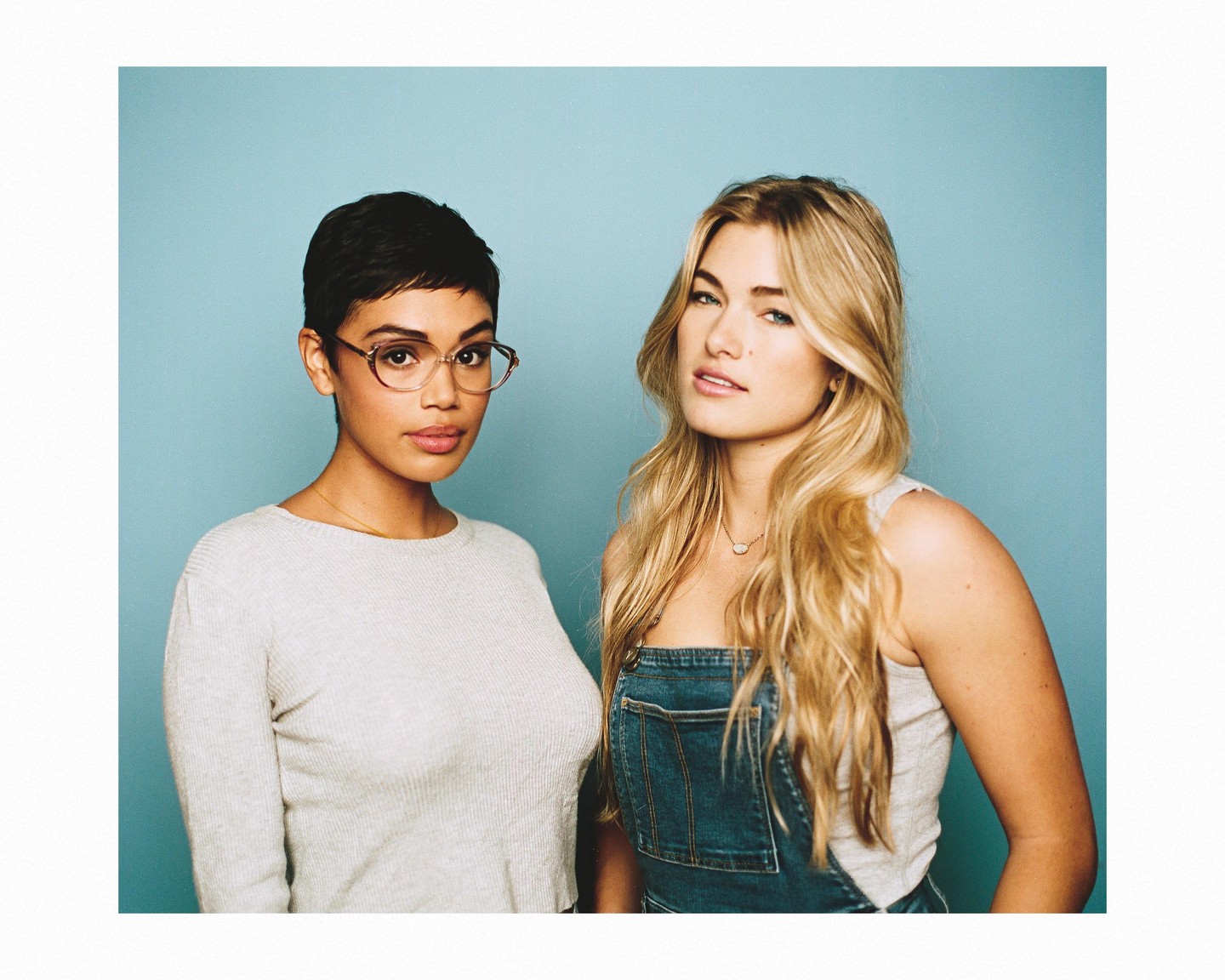 Two women pose for a portrait against a blue background.