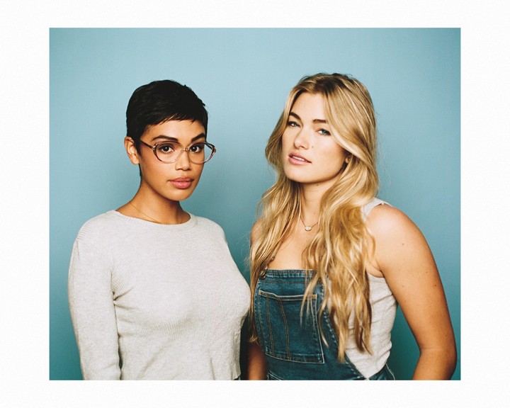 Two women pose for a portrait against a blue background.