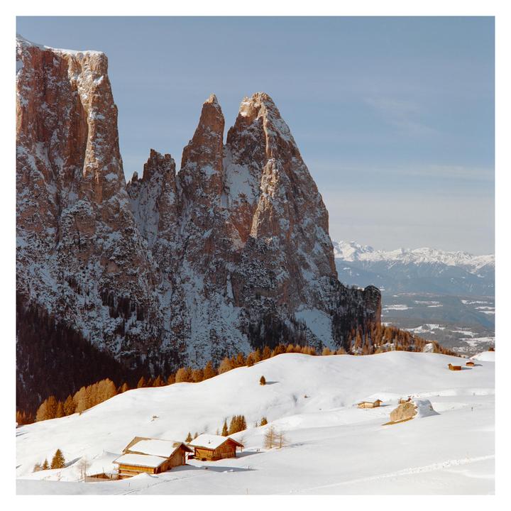 Snow-covered mountains rise above a valley with small wooden houses.