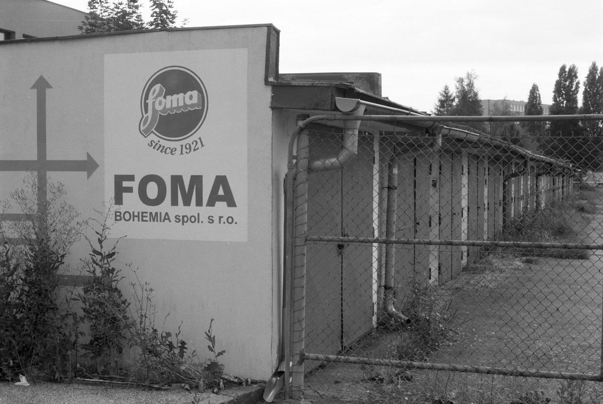 A Foma Bohemia sign is visible on a building next to a row of garages behind a chain link fence.