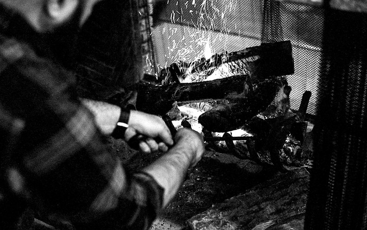 A man tends to a fireplace with sparks flying from the burning logs.