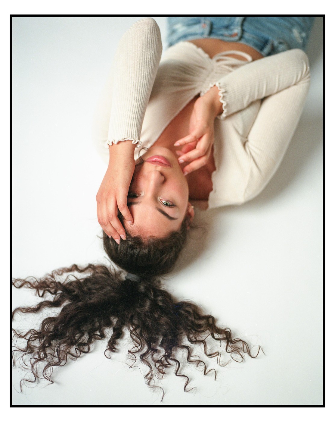 A woman with curly hair lies on her back, looking up at the viewer.