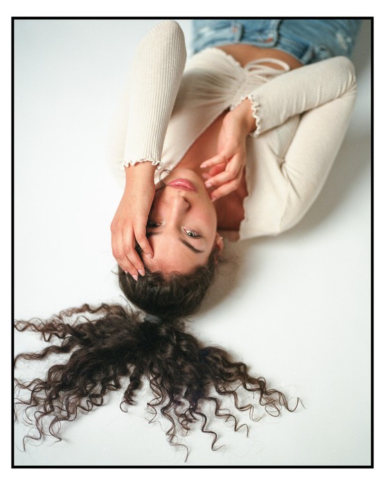 A woman with curly hair lies on her back, looking up at the viewer.