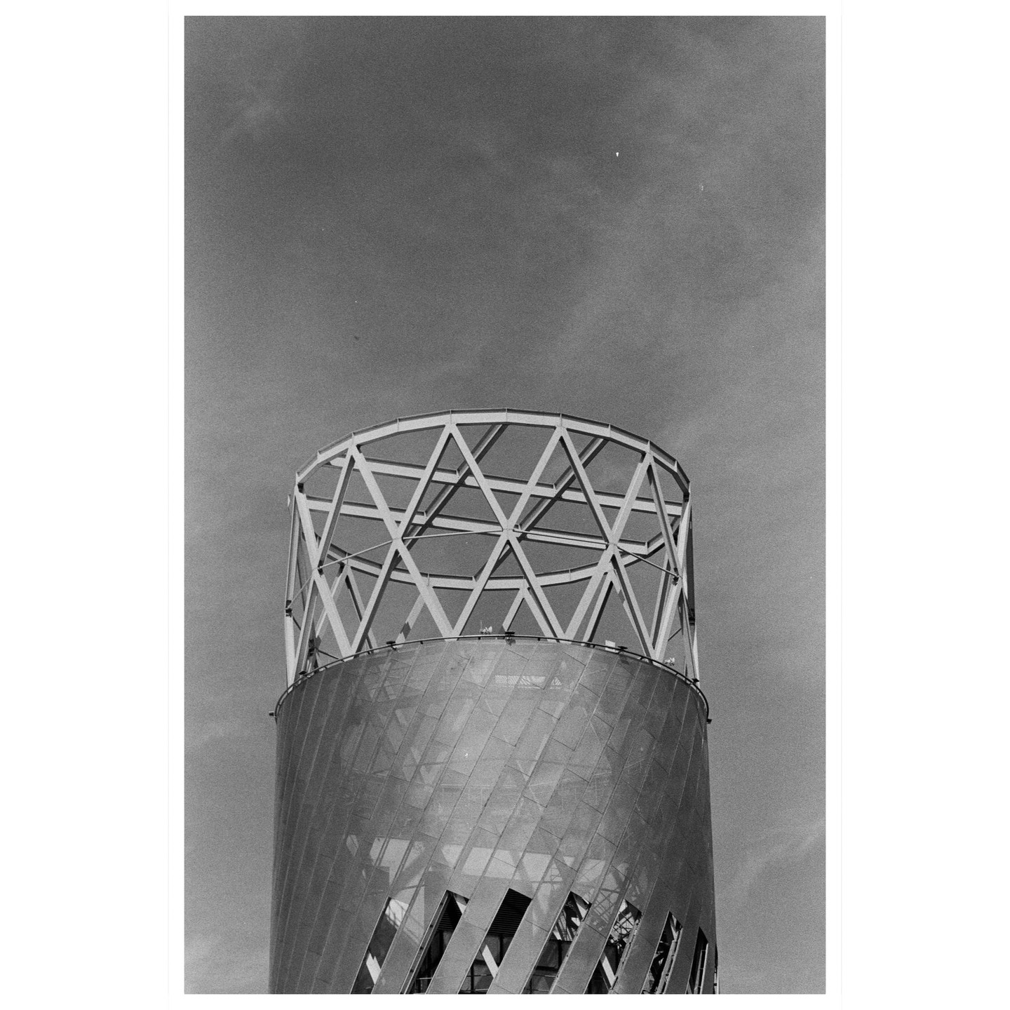 A cylindrical building with a geometric metal top stands against a cloudy sky.