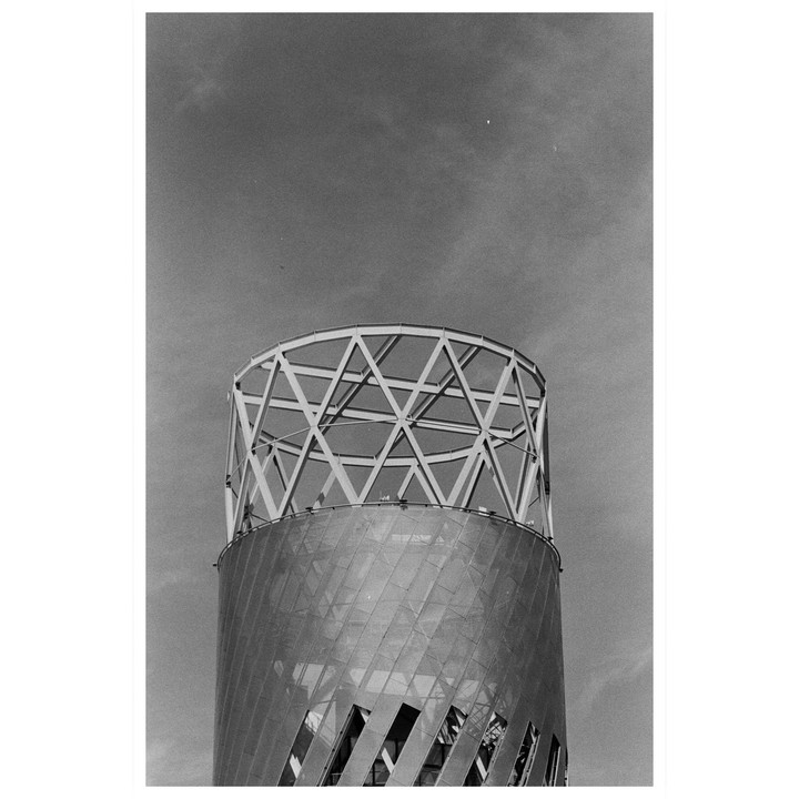 A cylindrical building with a geometric metal top stands against a cloudy sky.