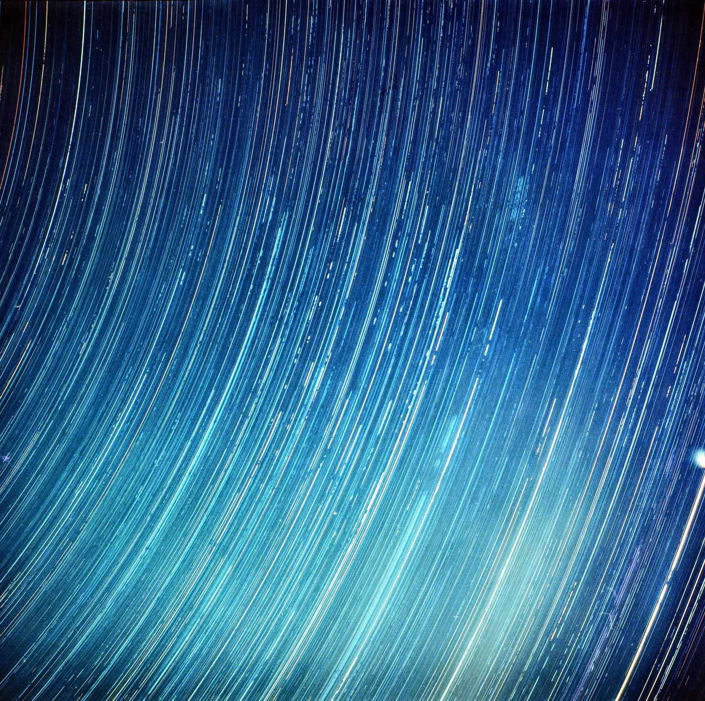 A long exposure photograph captures the movement of stars across a blue night sky, creating streaks of light.