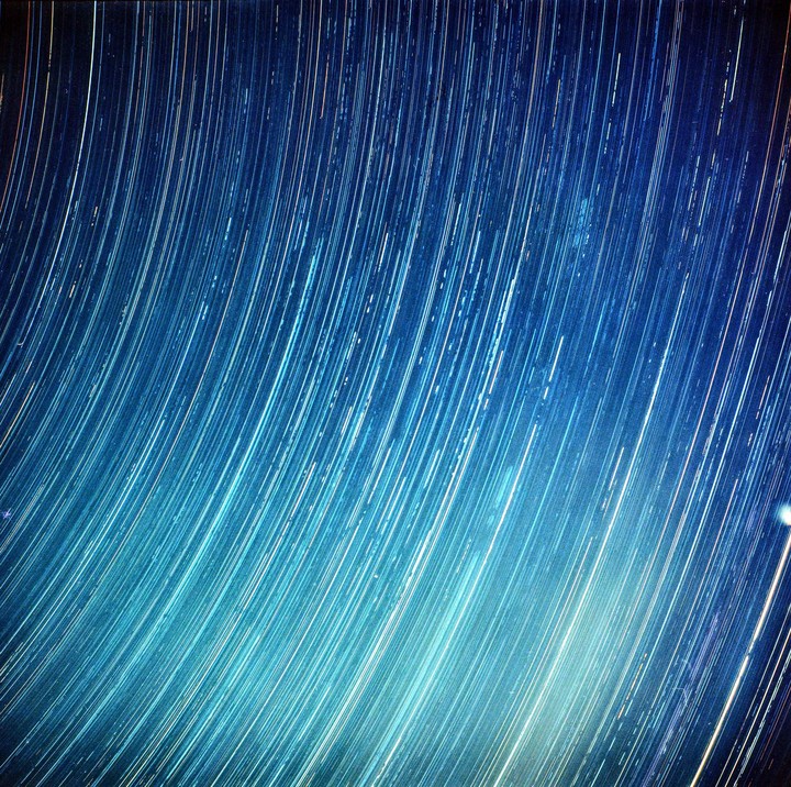 A long exposure photograph captures the movement of stars across a blue night sky, creating streaks of light.